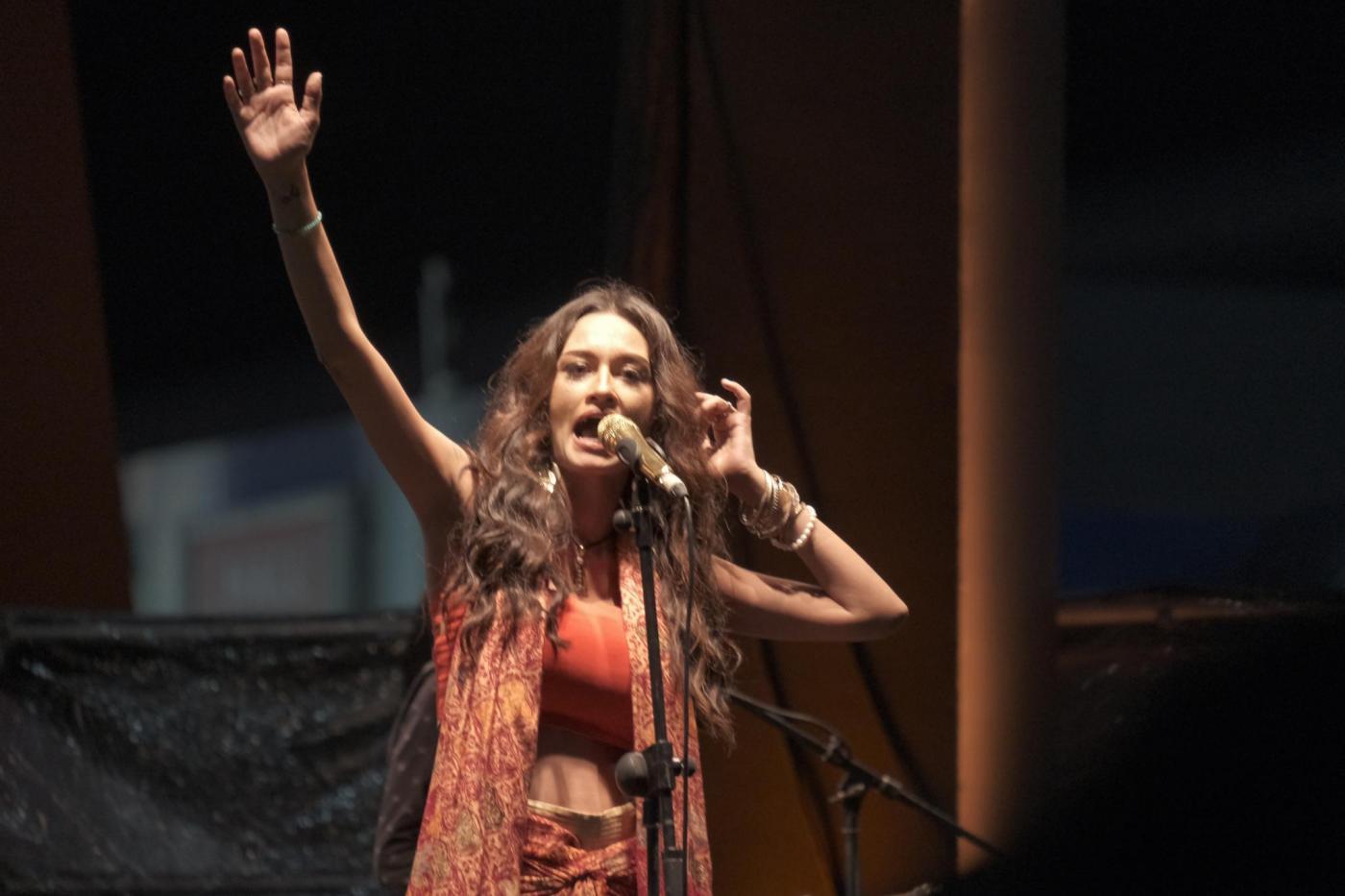 Rebecca Reijman menggunakan baju berwarna merah nata sedang menyanyi dengan mengangkat tangannya